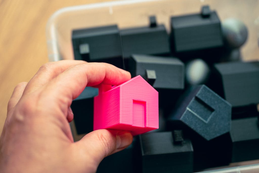 Hand selecting a pink house model from a box of miniature homes, symbolizing real estate choices.